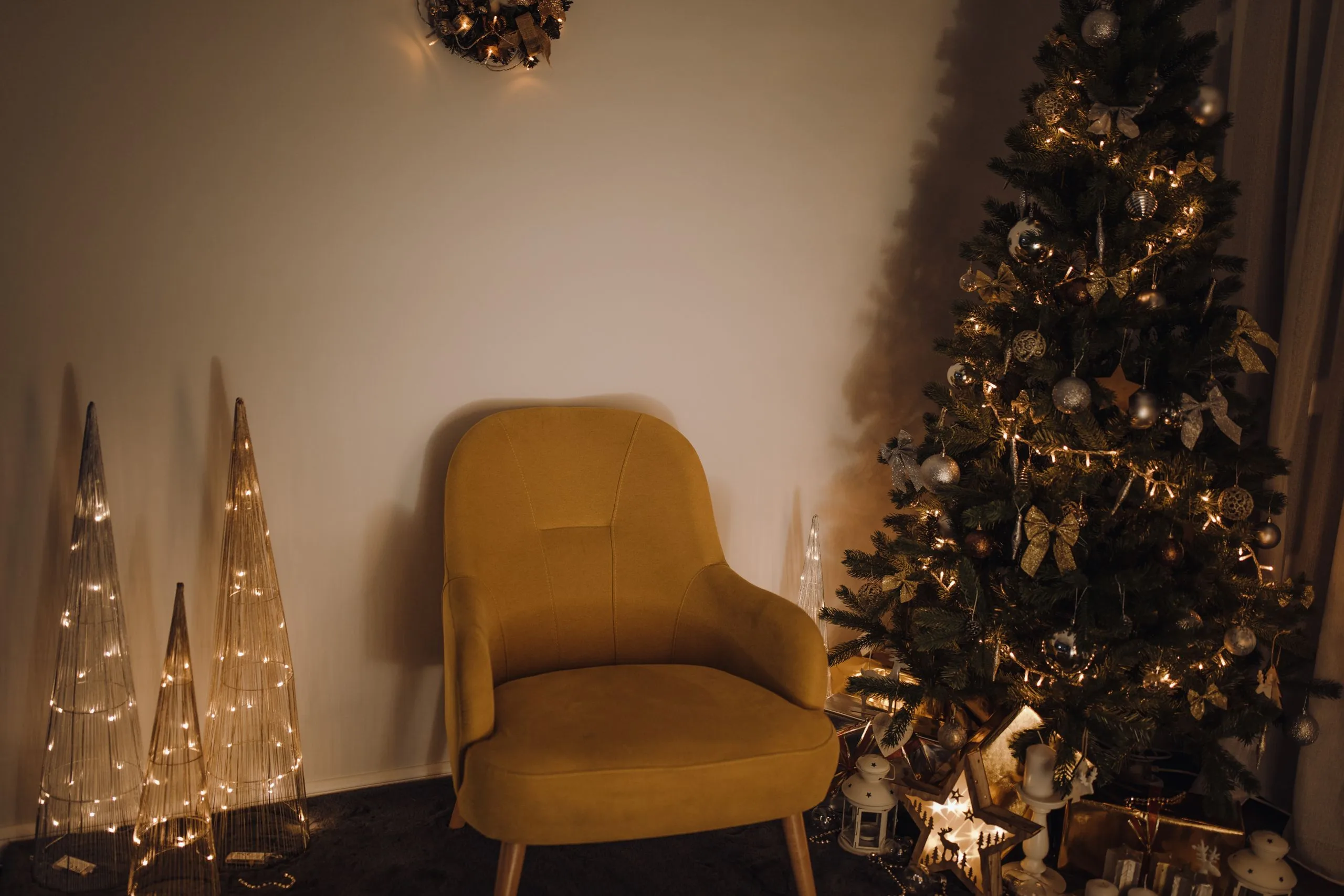 Salon décoré pour Noël avec sapin illuminé, guirlandes dorées et coussins rouges dans un style chaleureux.